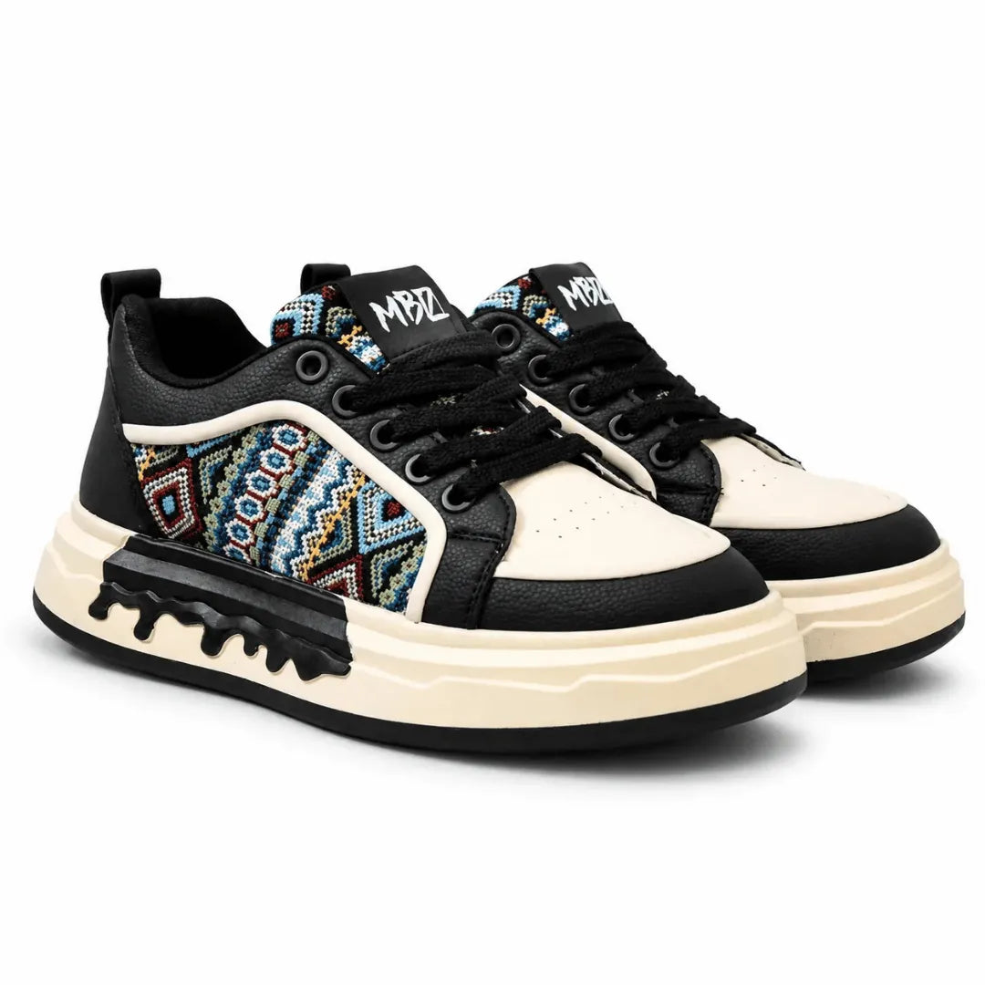 A pair of low-top sneakers with black and cream leather panels, a colorful geometric pattern on the side, black laces, and chunky cream and black soles, shown on a white background.