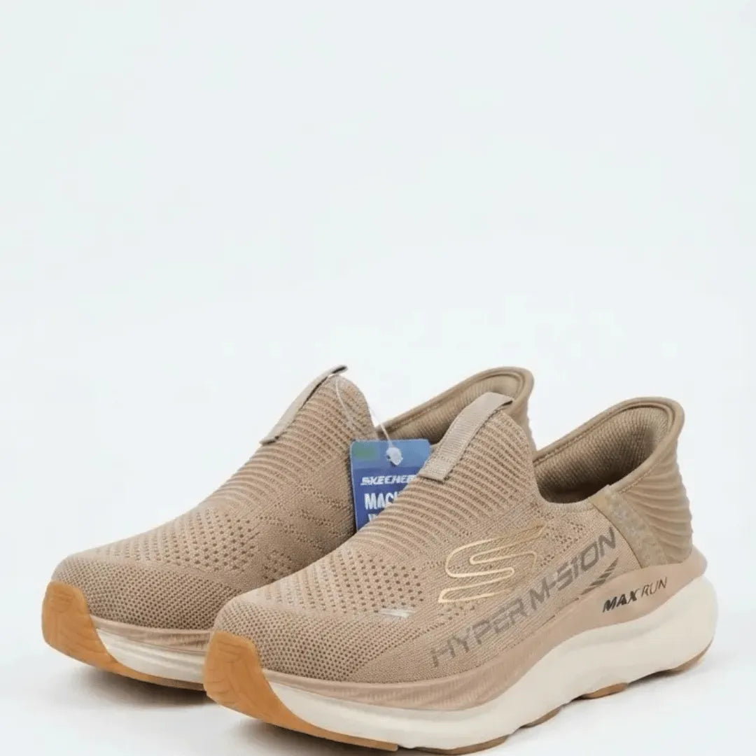 A pair of Skechers HyperMotion MAX-RUN slip-on sneakers in a light taupe-beige colorway, featuring a textured knit upper, a gold S logo, and a thick cream midsole.