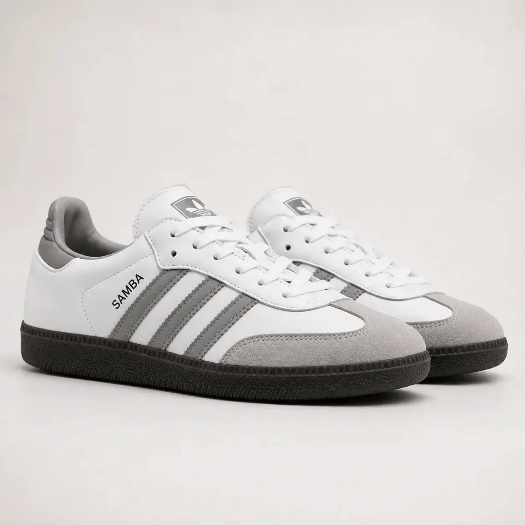 A pair of Adidas Samba sneakers in white and gray suede and leather, featuring the signature three stripes and black soles, photographed on a light gray studio background.
