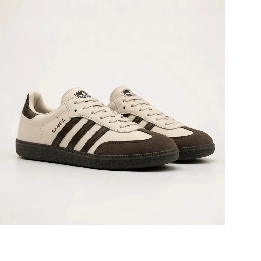 A pair of low-top Adidas Samba sneakers in beige and dark brown suede, featuring the signature three stripes and 'SAMBA' text on the side, set against a plain light gray background.