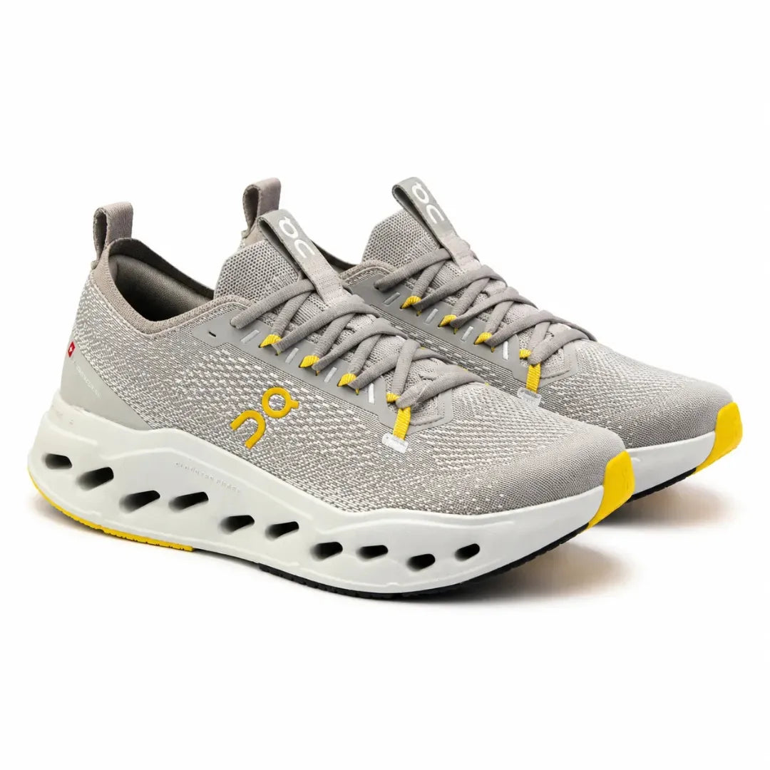 A pair of On Cloudrunning shoes in light gray with yellow accents and a white cushioned sole, shown on a clean white background.