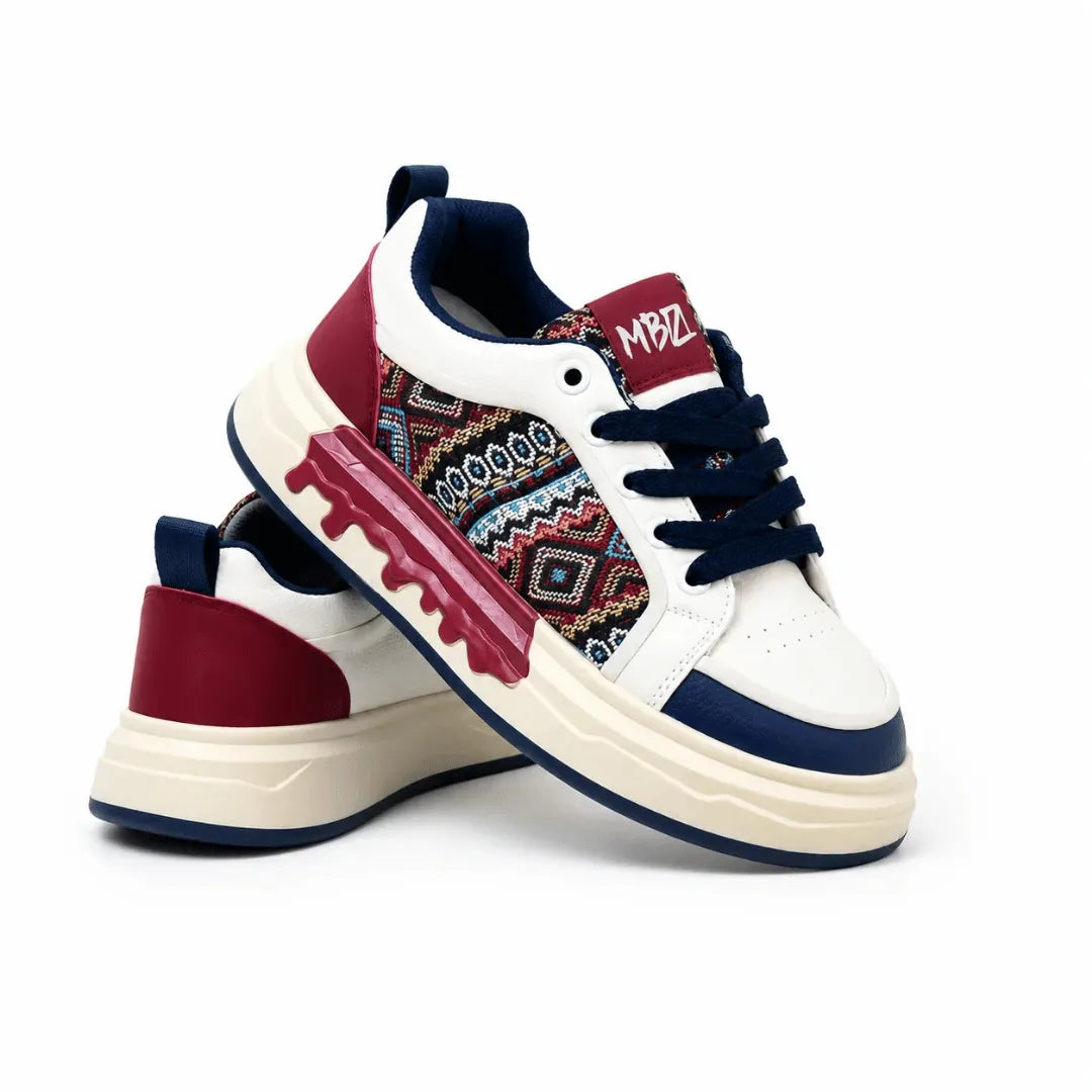 A pair of low-top sneakers on a white background. The shoes feature a white leather upper with navy blue accents, a burgundy heel tab, and a multicolor geometric pattern panel on the side.