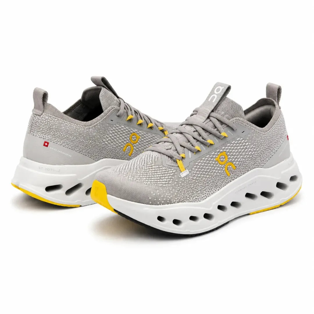 A pair of On Cloudrunning shoes in light gray knit with yellow accents, a white cushioned sole, and black interior lining, shown on a white background.