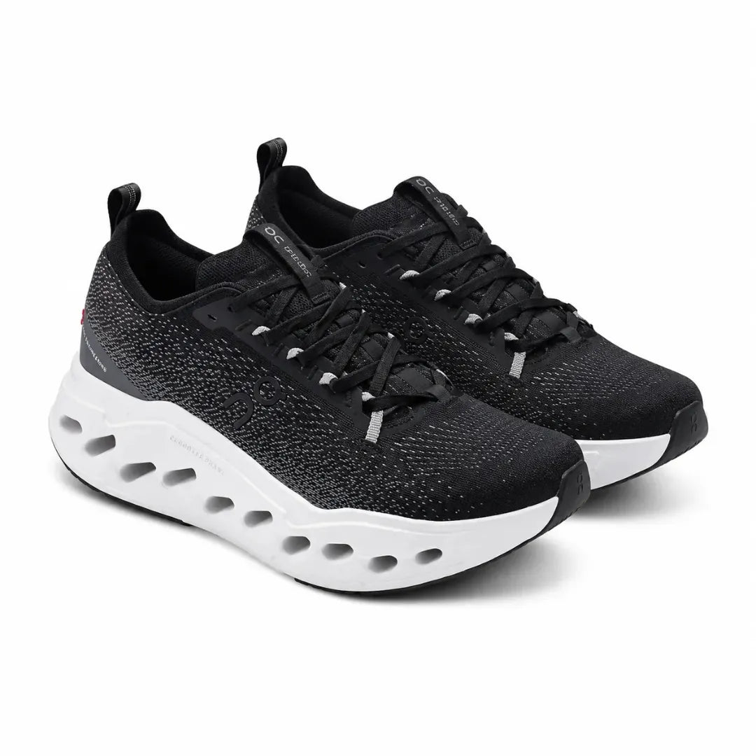 A pair of black athletic sneakers with a textured knit upper, black laces, and a thick white cushioned sole with circular cutouts, shown on a white background.