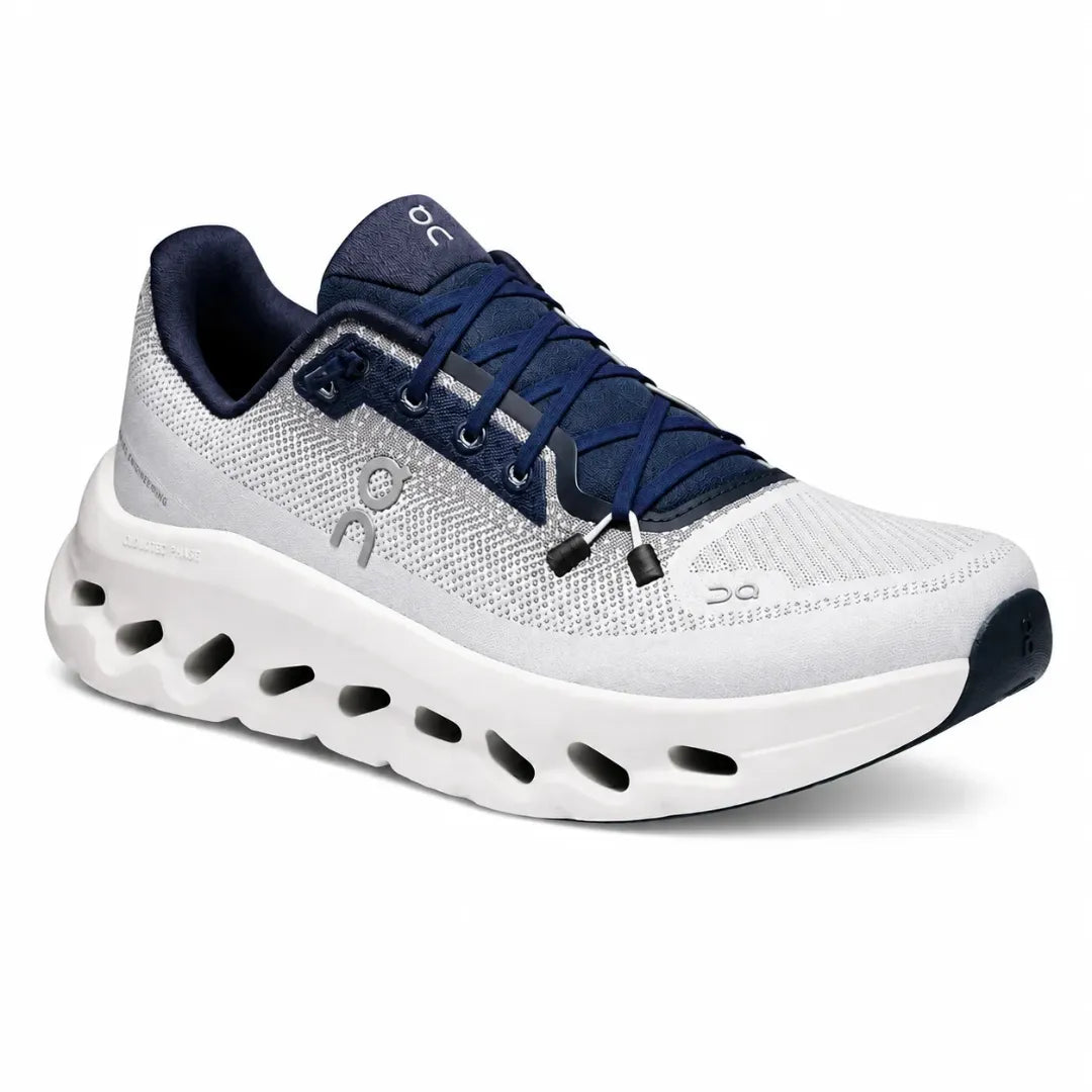 A white and navy blue On running shoe with a chunky, cushioned sole featuring multiple cutouts, shown from a three-quarters angle on a white background.