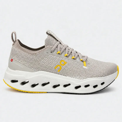 A light gray knit running shoe with a thick white and yellow sole, featuring yellow accents on the laces and logo, photographed against a light gray background.