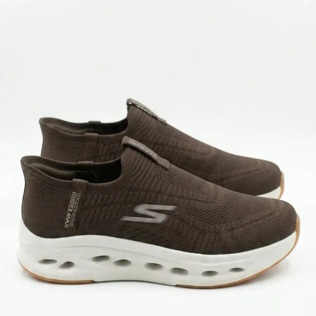 A pair of dark brown slip-on sneakers with a textured knit upper, a gray SKECHERS logo on the side, and a thick white cushioned sole, shown against a plain white background.