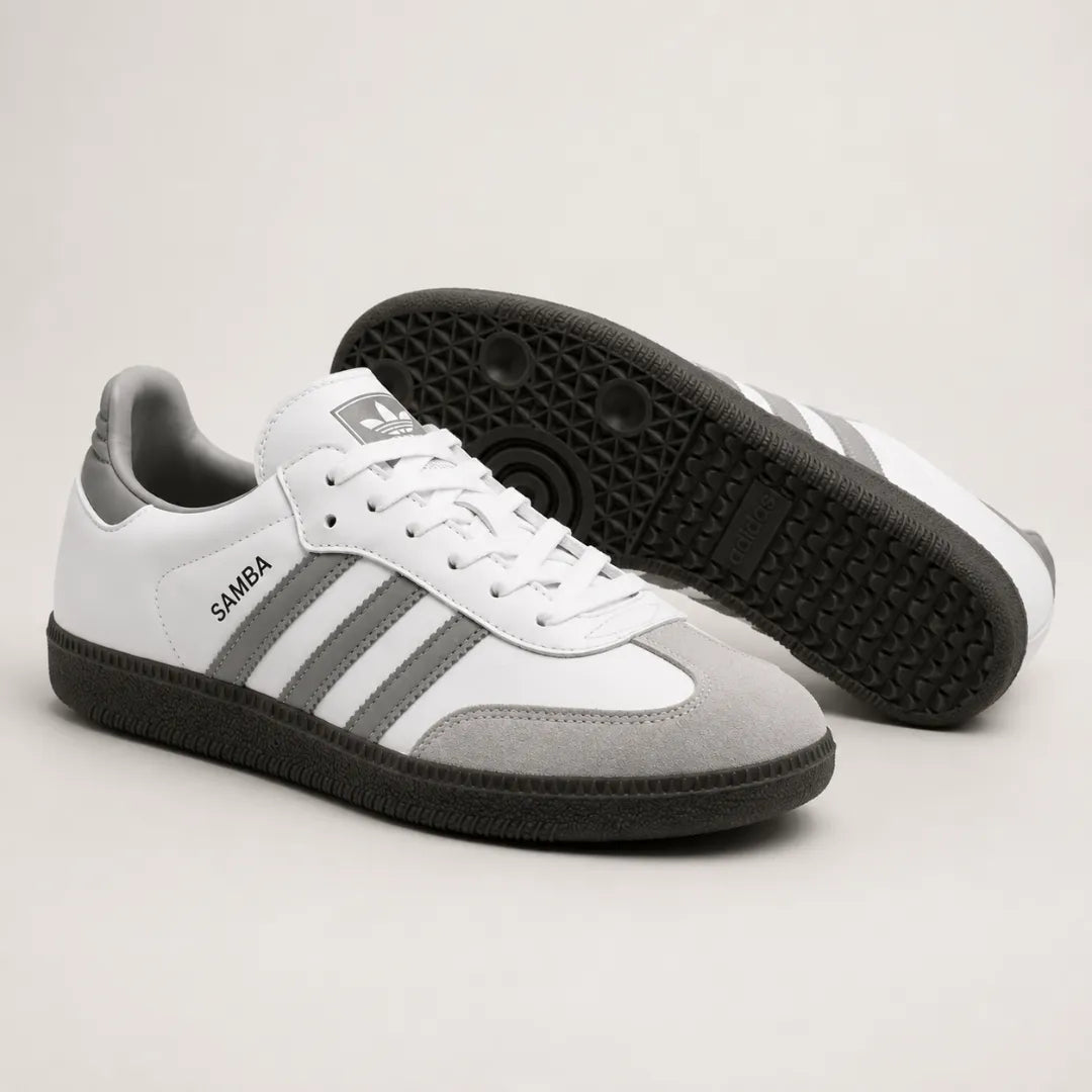 A pair of Adidas Samba sneakers in white, gray, and black, with one shoe showing the side profile and the other showing the black textured outsole.