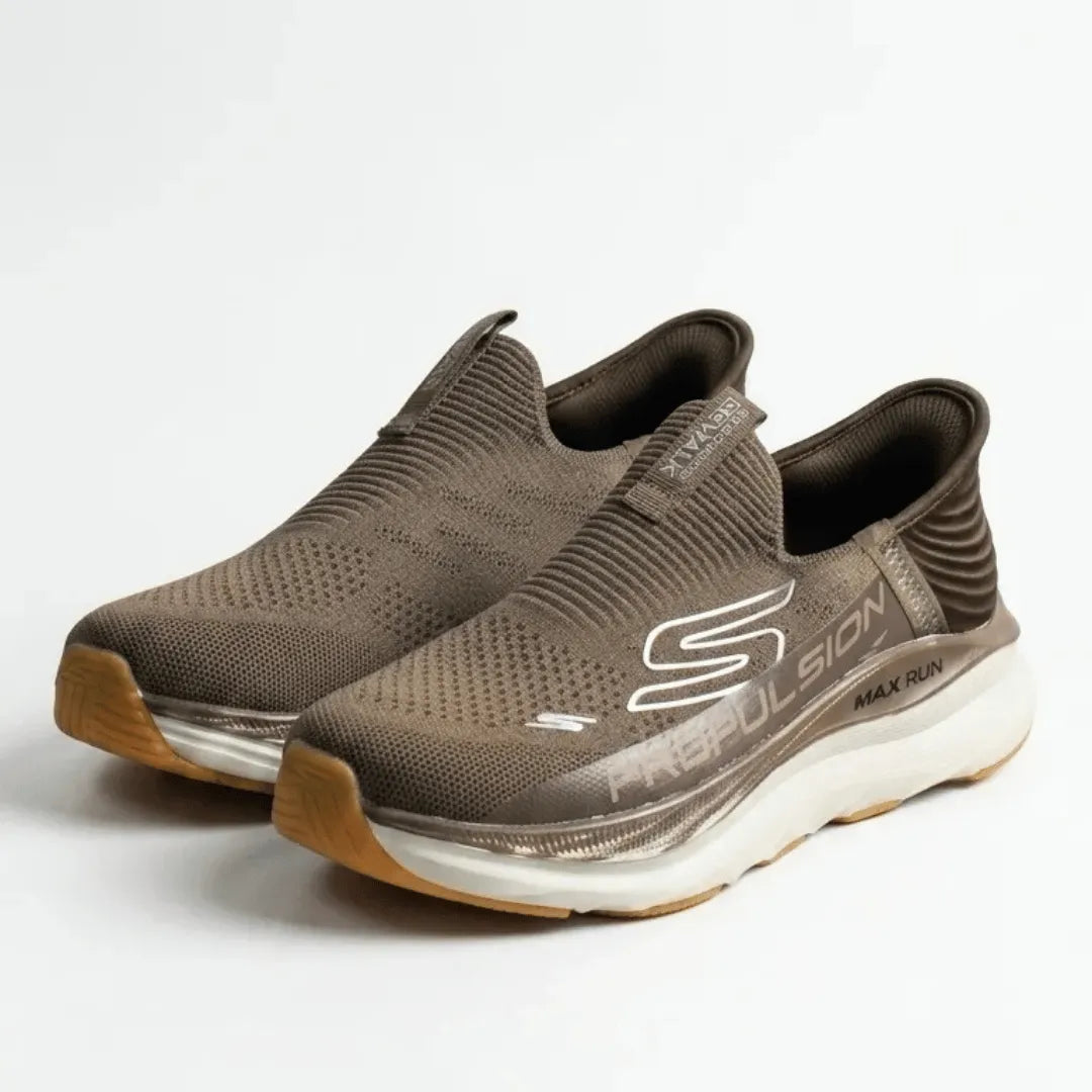 A pair of Skechers Pegasus Max Run slip-on sneakers in a dark brown colorway, featuring a textured knit upper, a white and brown midsole, and a gum outsole.