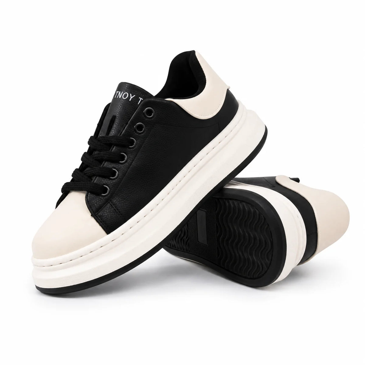 A pair of low-top platform sneakers in black and off-white, with one shoe standing upright and the other lying on its side to show the sole. The shoes are photographed on a clean white background.